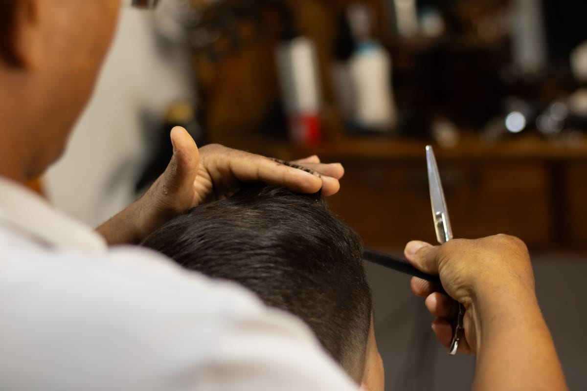 Kapper knipt met schaar en kam het haar van een klant, van achteren gezien