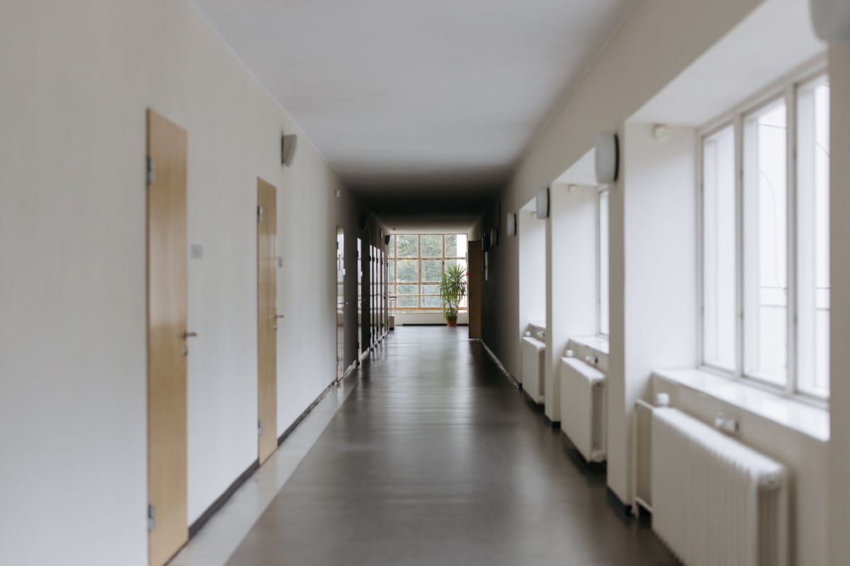 Lange lichte gang met houten deuren, radiatoren onder de ramen en een glanzende vloer