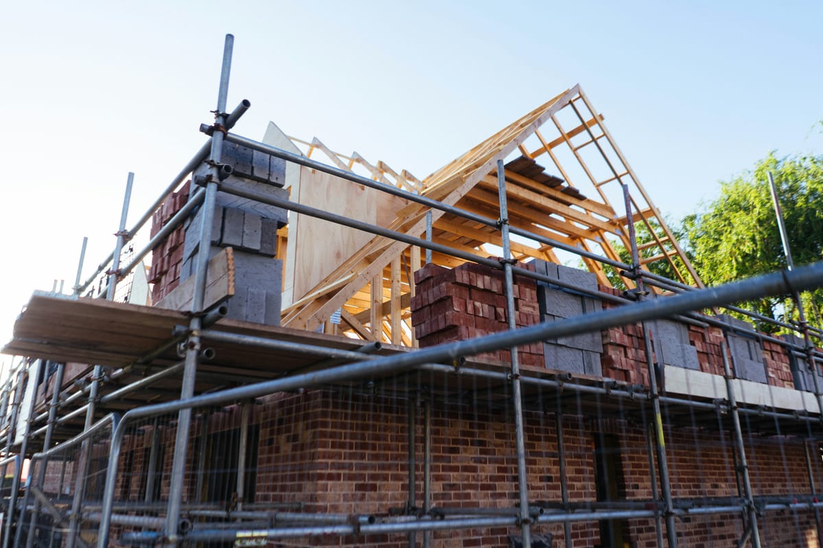 Woning in aanbouw met steigers, metselwerk en houten dakspanten