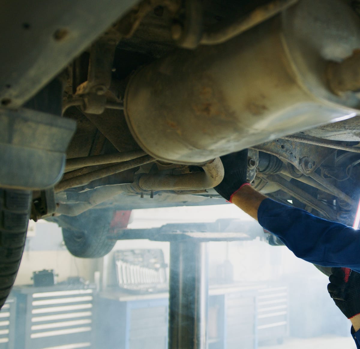 Mechaniker im blauen Overall arbeitet unter einem Auto auf der Hebebühne in einer hellen Werkstatt