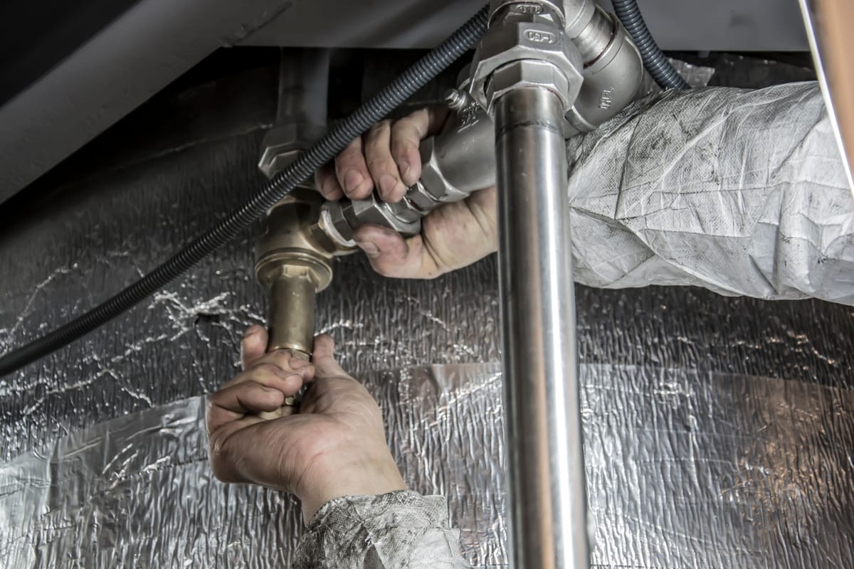 Hands tightening a coupling on pipes in front of an insulated wall