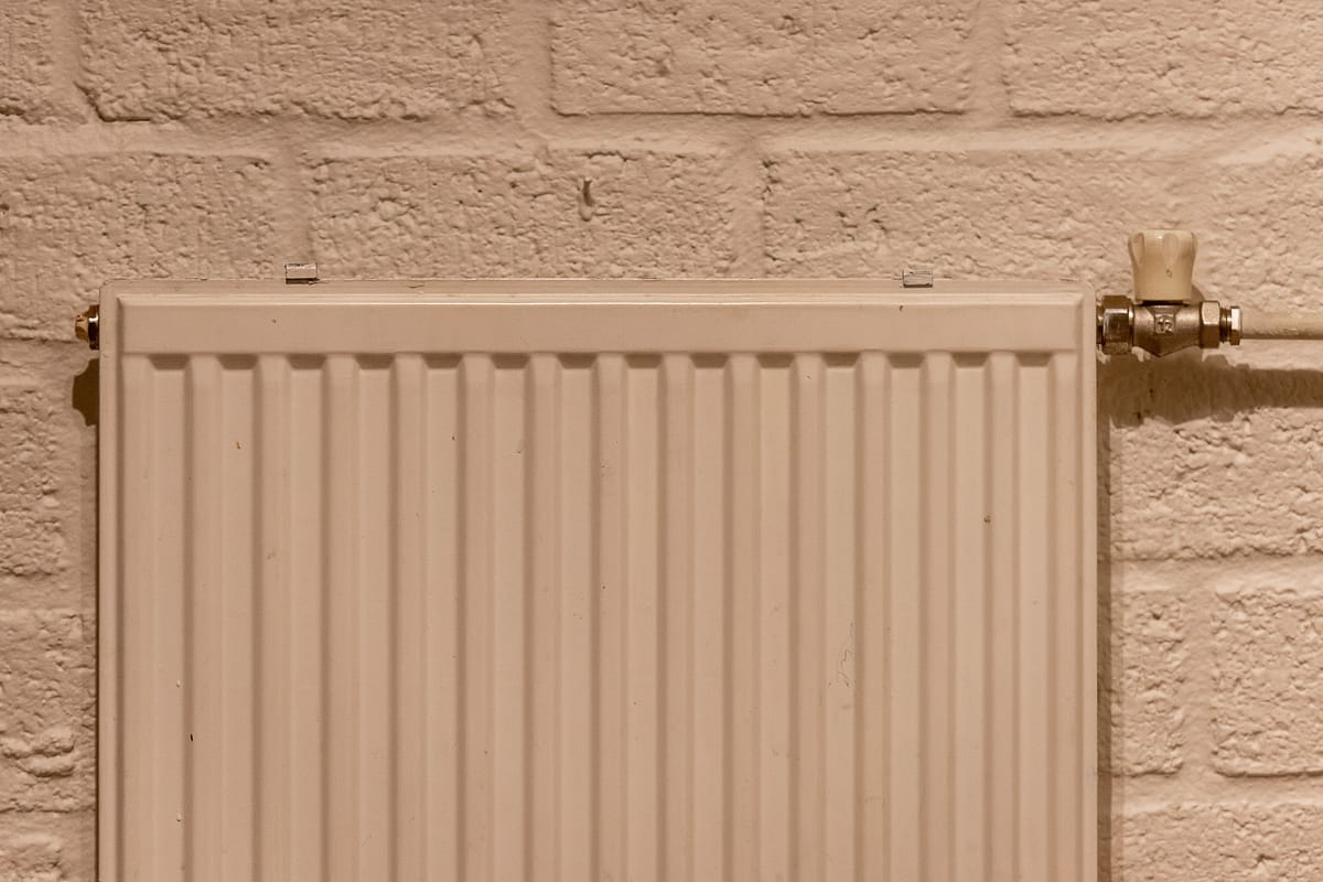 White panel radiator with a radiator valve against a light brick wall