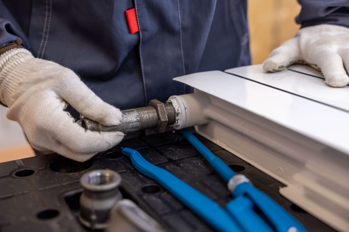 Hands in work gloves connecting a pipe to a radiator