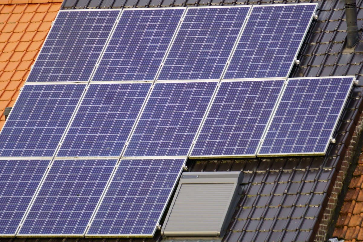 Solar panels on a dark tiled roof next to a roof window