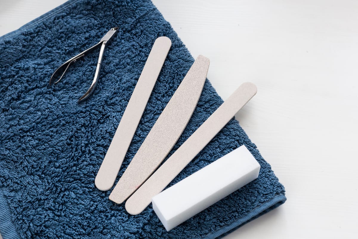 Une pince à ongles, trois limes et un bloc polissoir sur une serviette bleue