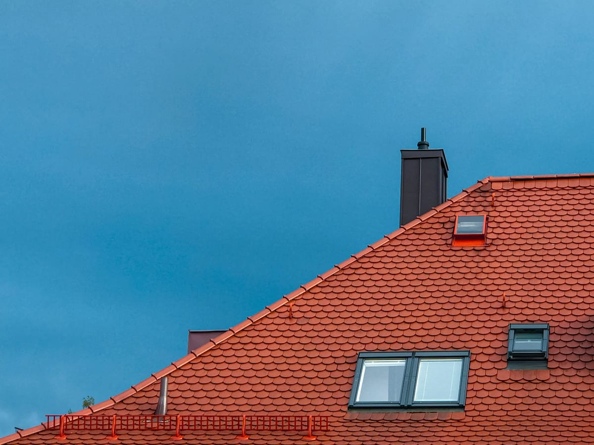 Rood pannendak met dakramen en schoorsteen onder een donkere lucht