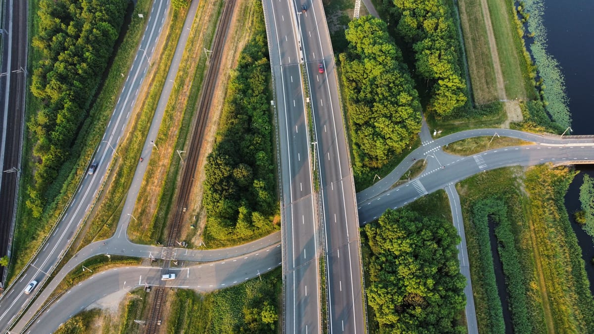 Luftaufnahme eines Autobahnkreuzes zwischen Bäumen und einem Graben in der Abendsonne