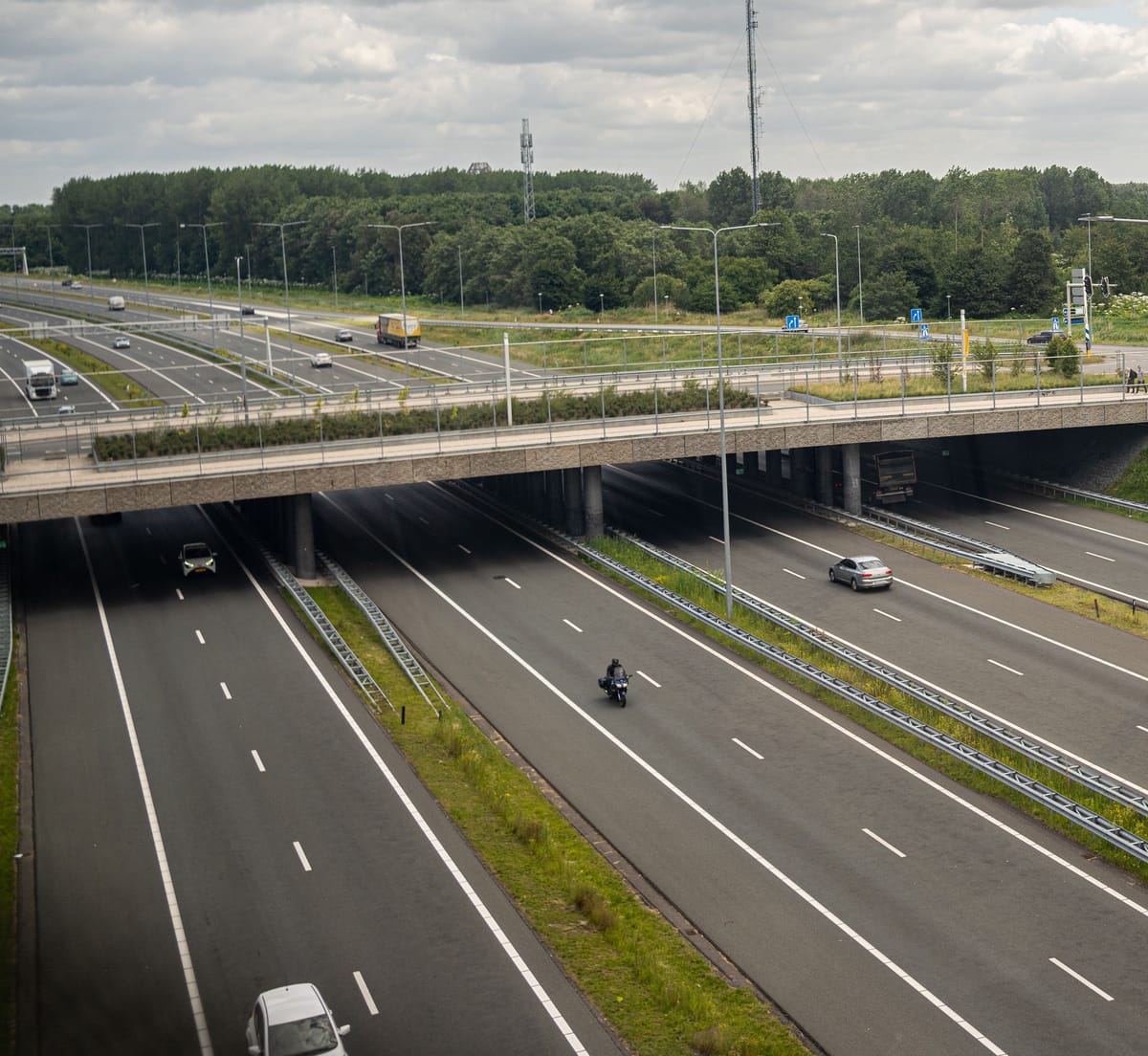 Eine Autobahn tagsüber unter einem Viadukt, mit einem Motorrad und ein paar Autos